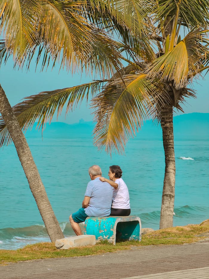 Elderly couple enjoying relaxation under palm trees by the turquoise sea on a sunny day